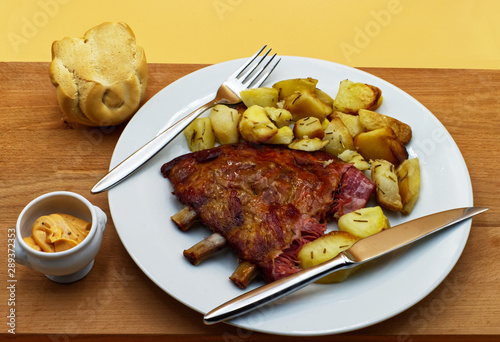 Grilled spare pork ribs with roasted potatoes, bread and sauce, on wooden table