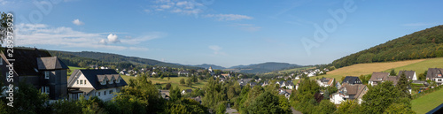 Wide panorama of a valley in Sauerland, Germany, with the spa village of Graftschaft and the pilgrimage Wilzenberg mountain at sunrise