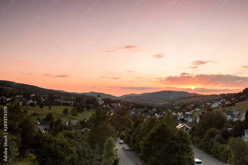 Wide panoramic view over the mountainous spa village of Grafschaft in the winter sports region of Sauerland, Germany, during sunset with a deep orange sky