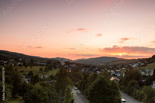 Wide panoramic view over the mountainous spa village of Grafschaft in the winter sports region of Sauerland, Germany, during sunset with a deep orange sky