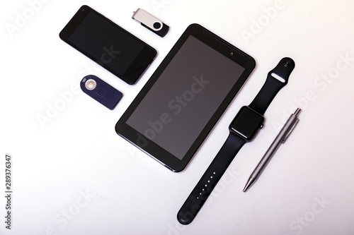 Business or education background. Tablet, phone, pendrive, pens, watch on white background. Set of black and silver accessories on white table, top view.