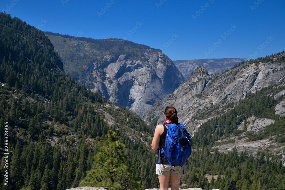 Young woman stands enjoying the view out over Yosemite National Park in the summer.