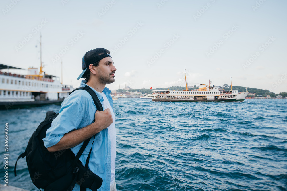 Portrait of a young man against the background of the sea, city, pier and ships.