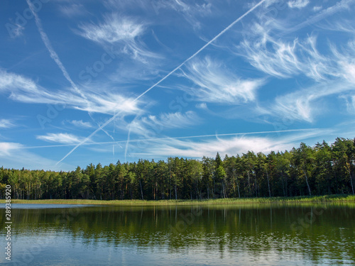 Lake shines green in summer under blowing clouds, white clouds of interesting shape reflect on lake surface, Lake Valdis, Turna, Latvia photo