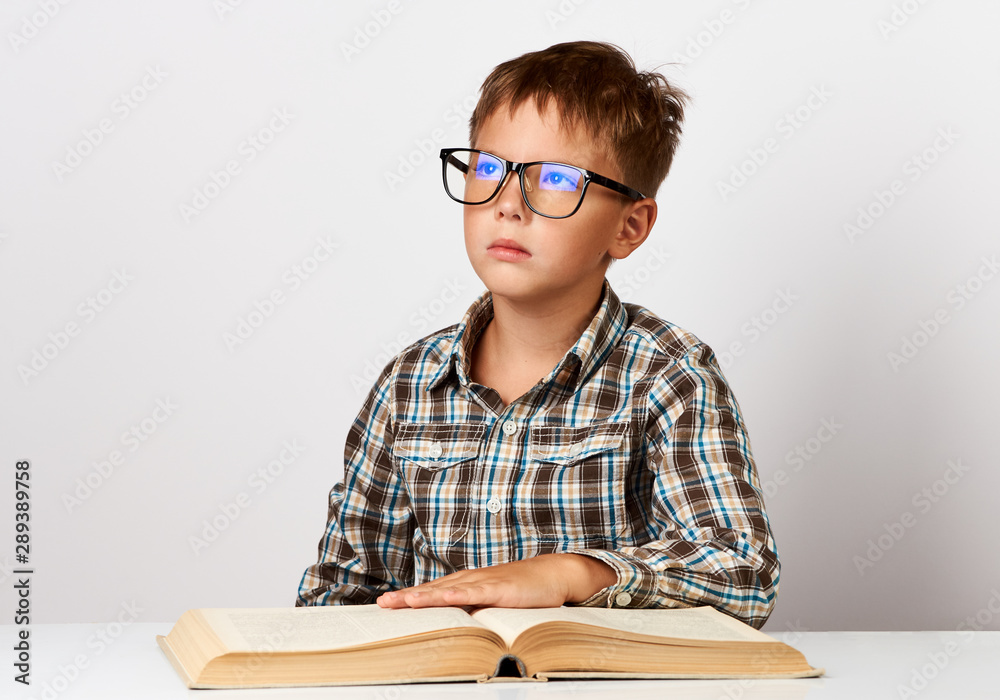 Cute little boy is sitting at desk with book. Seven years old child Cute little boy is sitting at desk with book. Seven years old child