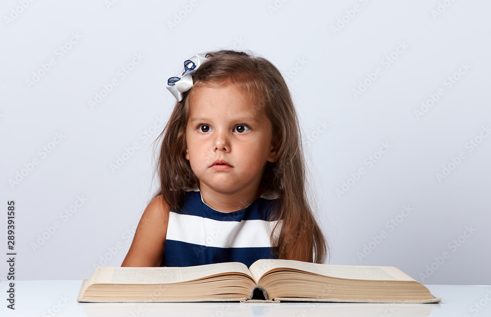 Cute little girl sitting at table with book over white background Cute little girl sitting at table with book over white background