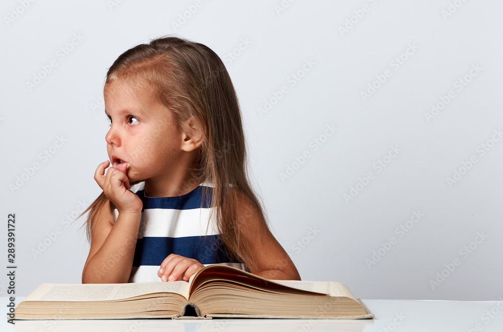 Cute little girl sitting at table with book over white background Cute little girl sitting at table with book over white background