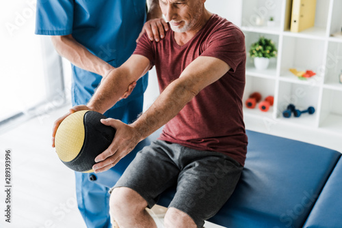 selective focus of bearded middle aged man exercising with ball near doctor