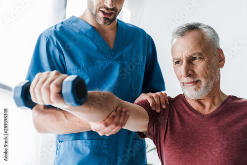 cropped view of doctor standing near mature man holding dumbbell photo