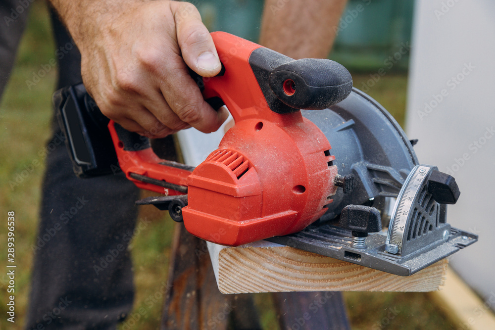 Building contractor worker using hand circular saw to cut boards on a new home constructiion project