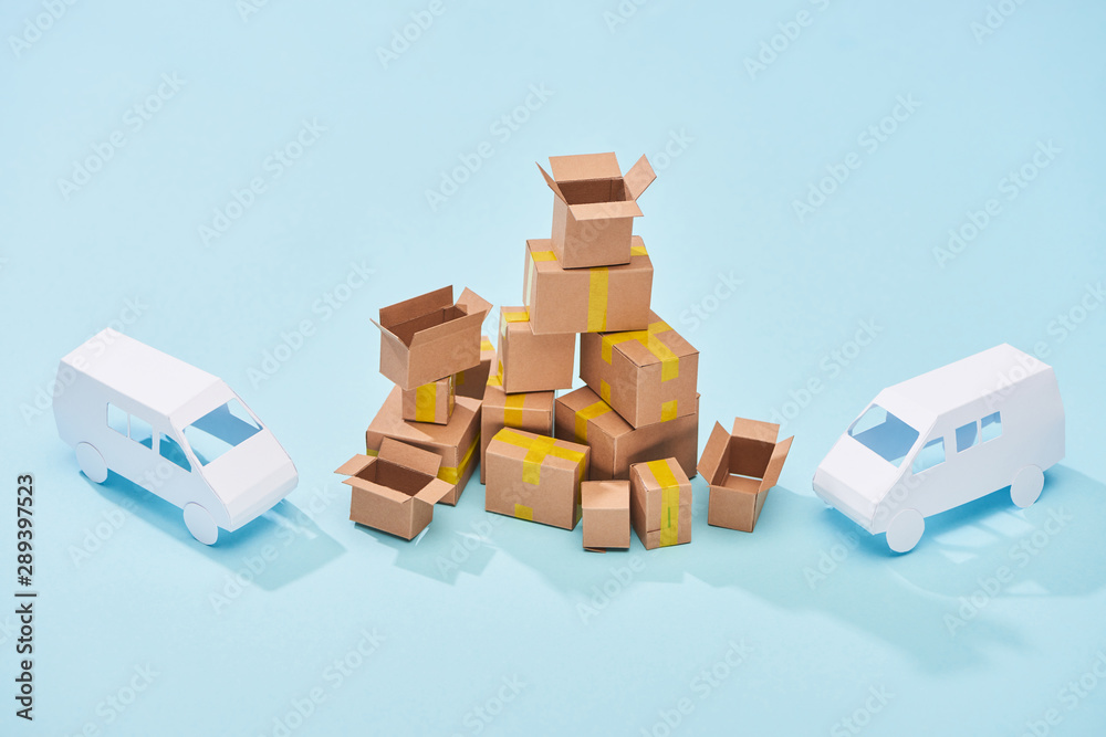 pile of cardboard boxes between white mini vans on blue background