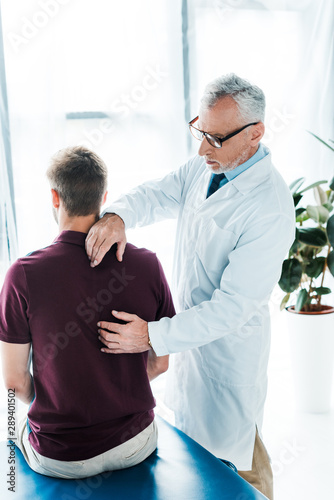 back view of patient sitting near chiropractor in clinic