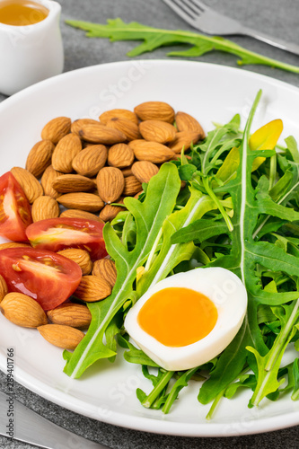 Arugula salad with almonds and tomato,boiled egg in white dish on tile table.