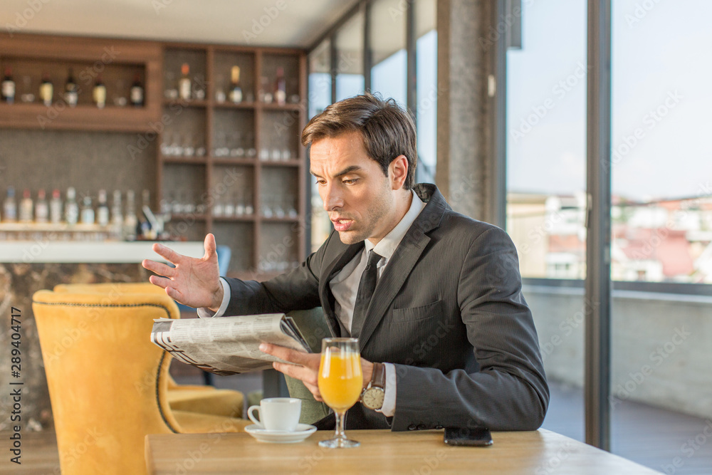 Handsome young businessman reading newspaper in hotel cafe Handsome young businessman reading newspaper in hotel cafe