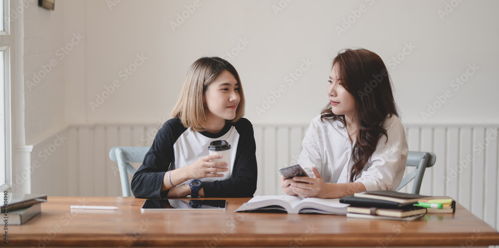 Two adorable young females chatting together while working on their project