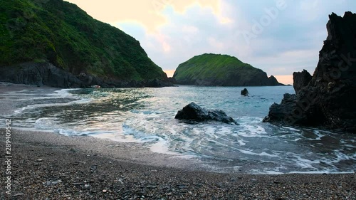 Sunrise Behind Coastal Cliffs With Low Camera Next to Water On Pebble Shoreline With Gentle Waves photo