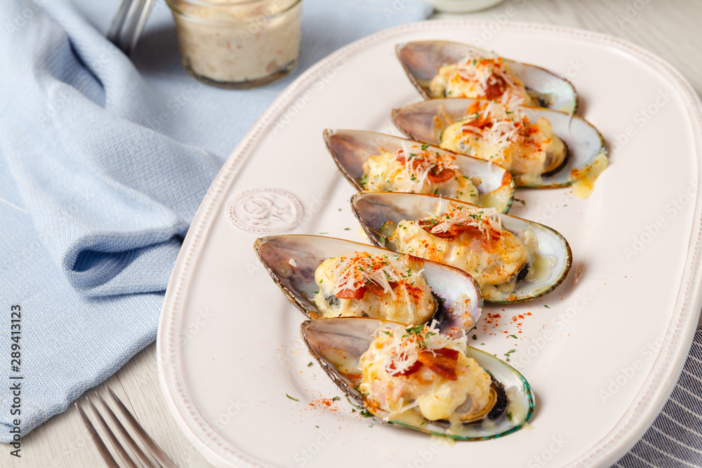Baked mussels with cheese and bacon on white dish.