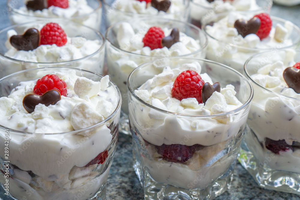 Fresh cream desserts in glasses with crumbles, a chocolate heart and one raspberry Fresh cream desserts in glasses with crumbles, a chocolate heart and one raspberry