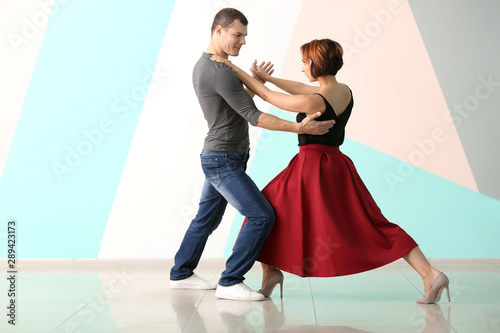 Cute loving couple dancing against color wall