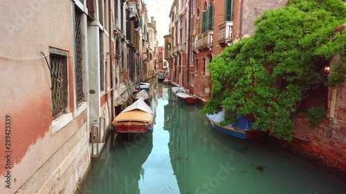VENICE, Italy - May 2019: Beautiful scenery of a venetian canal street. Turquoise water, moored boats. In the background are green trees. Italian style houses. Slow motion
