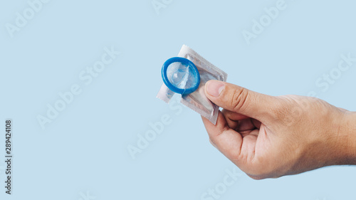 Close-up hand holding condom with blue background