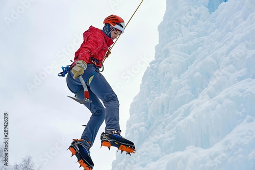Fotografi Alpinist woman with ice tools axe in orange helmet climbing a large wall of ice