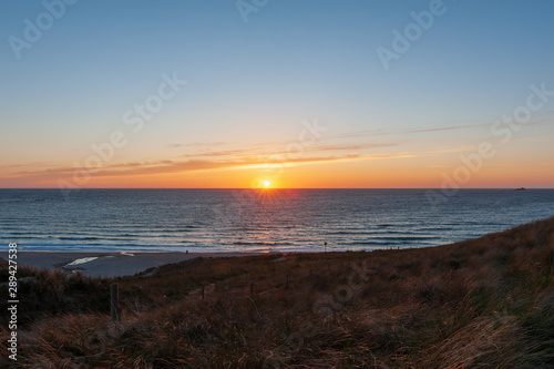 The sun sets in the far distance on the ocean as it casts beautiful golden colours over the clouds and skies above and turns the English landscape into a silhouette.