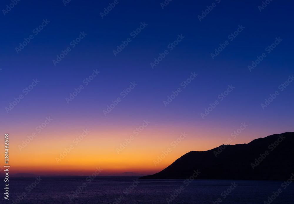 Twilight vibrant colorful sky above sea and mountain sihlouette at dusk time.