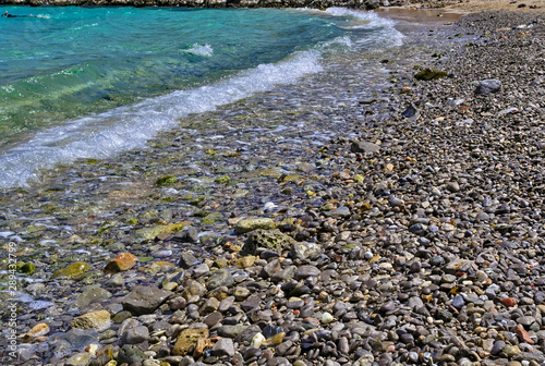 Stone beach low angle view, pebbles turquoise sea wate and snorkeler swimming.