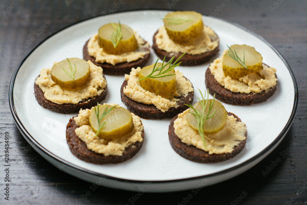 Pumpernickel rounds with hummus and pickled cucumber slices as snack. Pumpernickel rounds with hummus and pickled cucumber slices as snack.