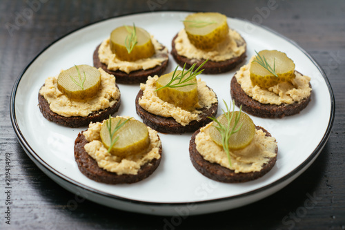 Pumpernickel rounds with hummus and pickled cucumber slices as snack.