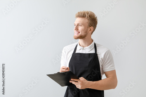 Naklejka Handsome waiter with clipboard on light background