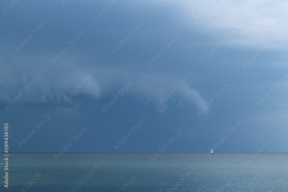 a small sailing boat drifts lost on the sea before a huge summer storm is coming