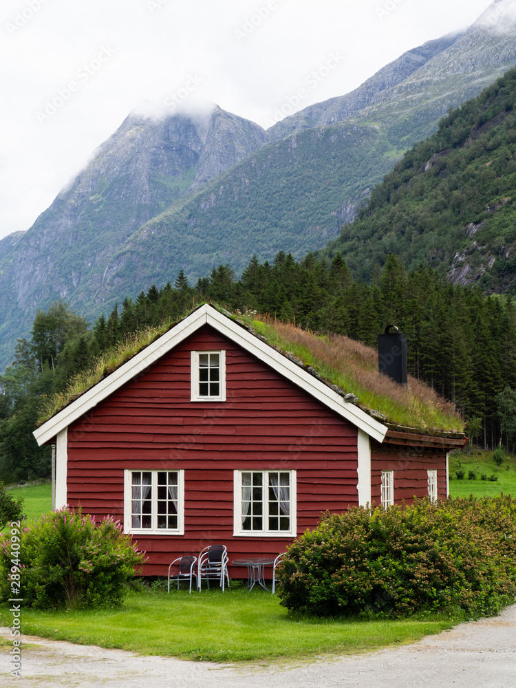 Traditional red wooden house with plants and grass on the roof. House in a green valley near a big mountain