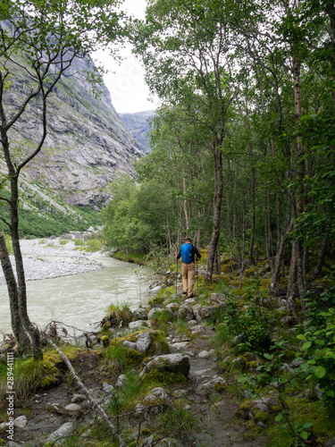 An indefinite man with tourist equipment is walking over stones in a forest in Norway. Hiking trail through the forest next to a mountain river and stones overgrown with moss