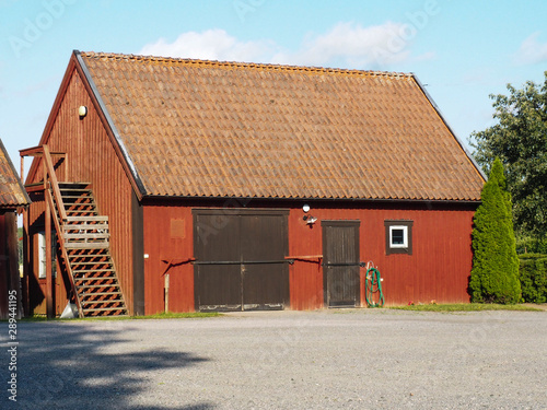 Red wooden barn with a gate and staircase. Large non-residential building in a large utility yard