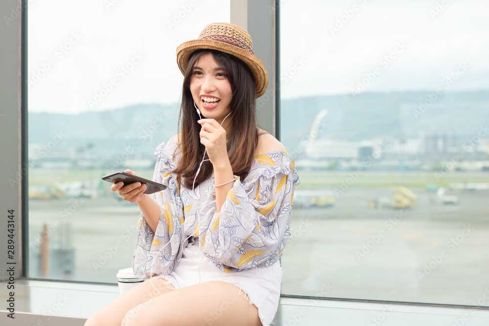 Beautiful young woman in earphones sitting outdoors, talking on mobile phone, drinking coffee.