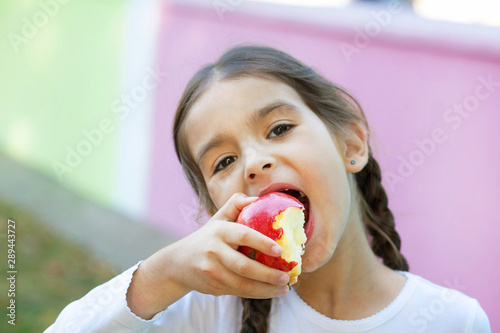 Cute little child girl eating apple outdoors