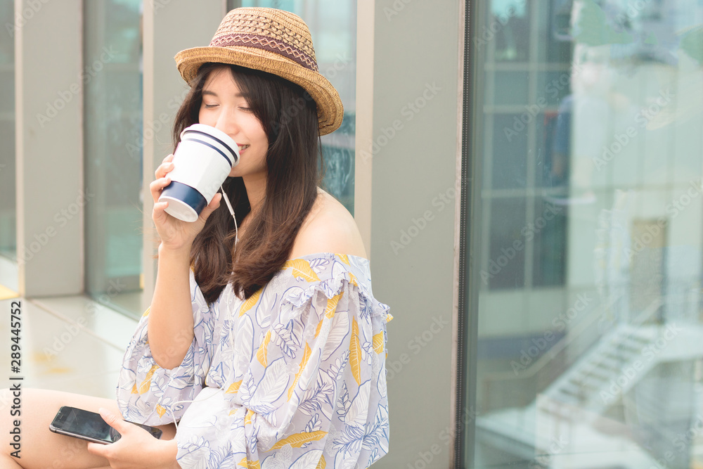 Relaxation and technology. Young asian woman drinks coffee and listens to the music by mobile phones.
