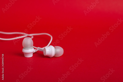 White headphones (earphones) on a red background with copy space close up © Fukume