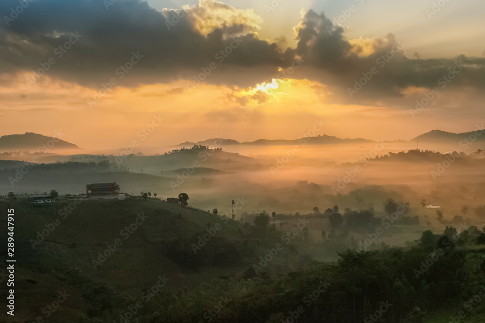 Obraz premium Mountain view misty morning of top hills around with sea of fog in valley and sun-rays in cloudy sky background, sunrise at Wat Kong Niam View Point, Khao Kho, Thailand.
