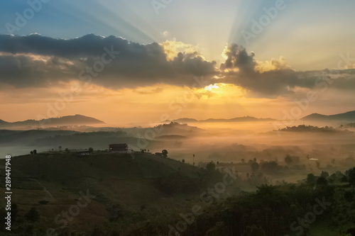 Mountain view misty morning of top hills around with sea of fog in valley and sun-rays in cloudy sky background, sunrise at Wat Kong Niam View Point, Khao Kho, Thailand.