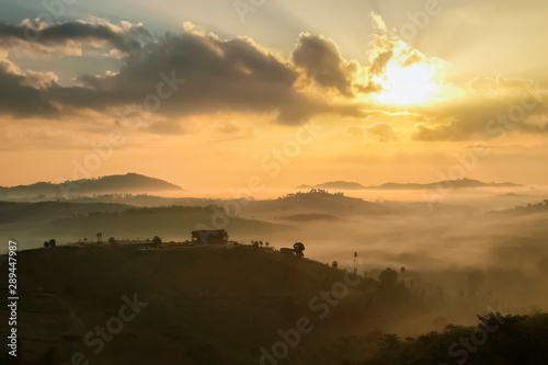 Mountain view morning of top hills and forest around with sea of fog with yellow sun light in the sky background, sunrise at Wat Kong Niam View Point, Khao Kho, Phetchabun, Thailand. © Yuttana Joe