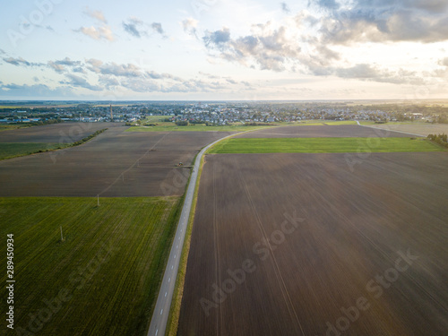 Aerial view of road surrounded by agricultural fields leading to small town in north of Lithuania - Joniskis