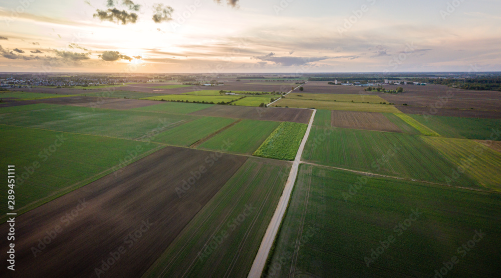 Aerial view of dirt road surrounded by agricultural fields and sunset in background