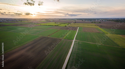 Aerial view of dirt road surrounded by agricultural fields and sunset in background