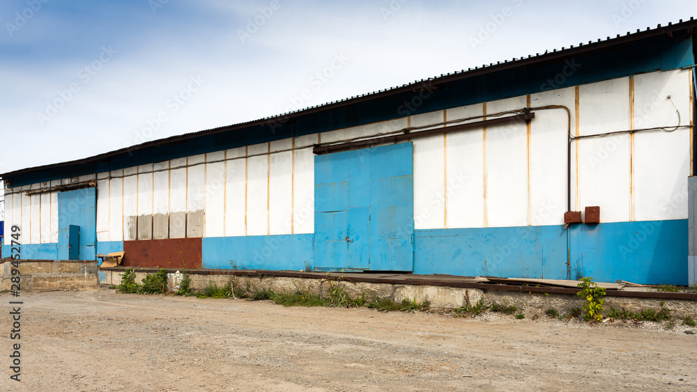Facade on large industrial building made of metal white and blue panels. Industrial concept of transportation, loading and storage of goods