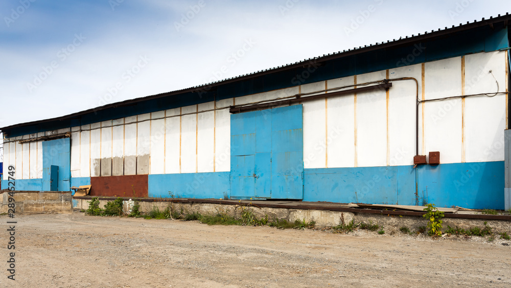 Facade on large industrial building made of metal white and blue panels. Industrial concept of transportation, loading and storage of goods Facade on large industrial building made of metal white and blue panels. Industrial concept of transportation, loading and storage of goods