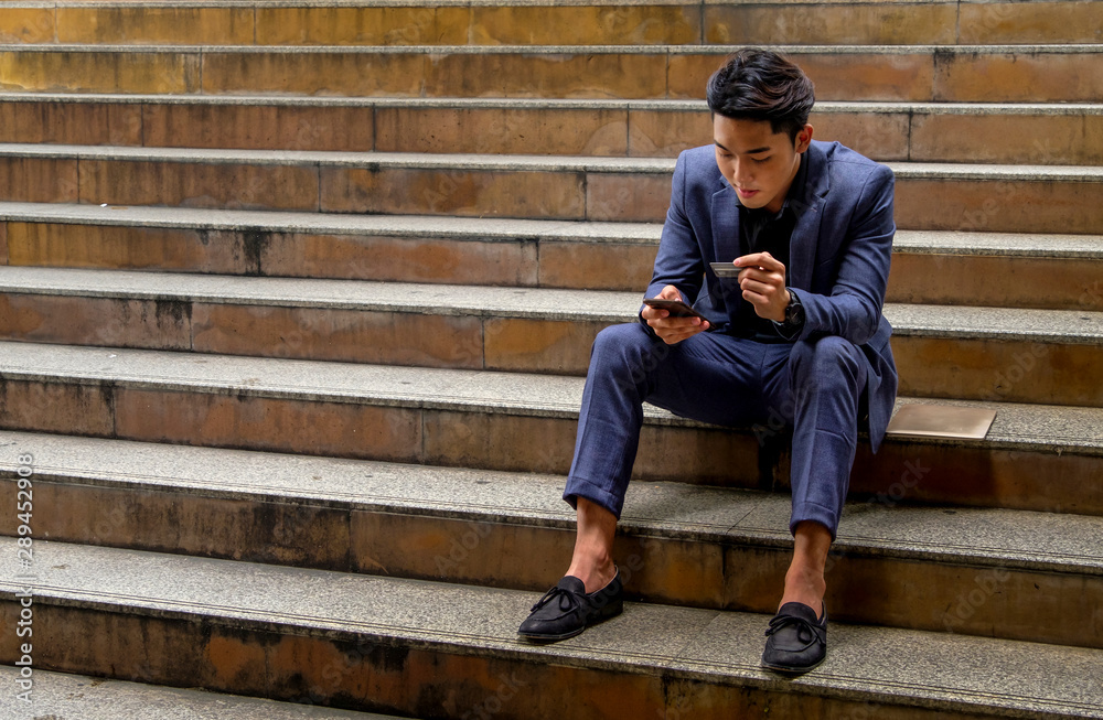 A young businessman sit using credit card for online shopping on mobile phone A young businessman sit using credit card for online shopping on mobile phone
