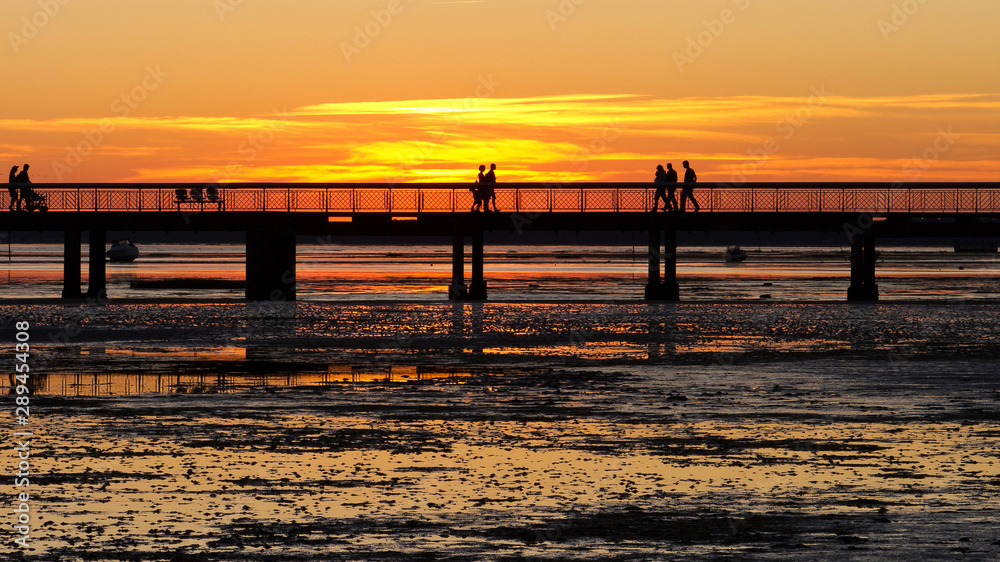 Silhouettes of people strolling on a jetty at sunset.